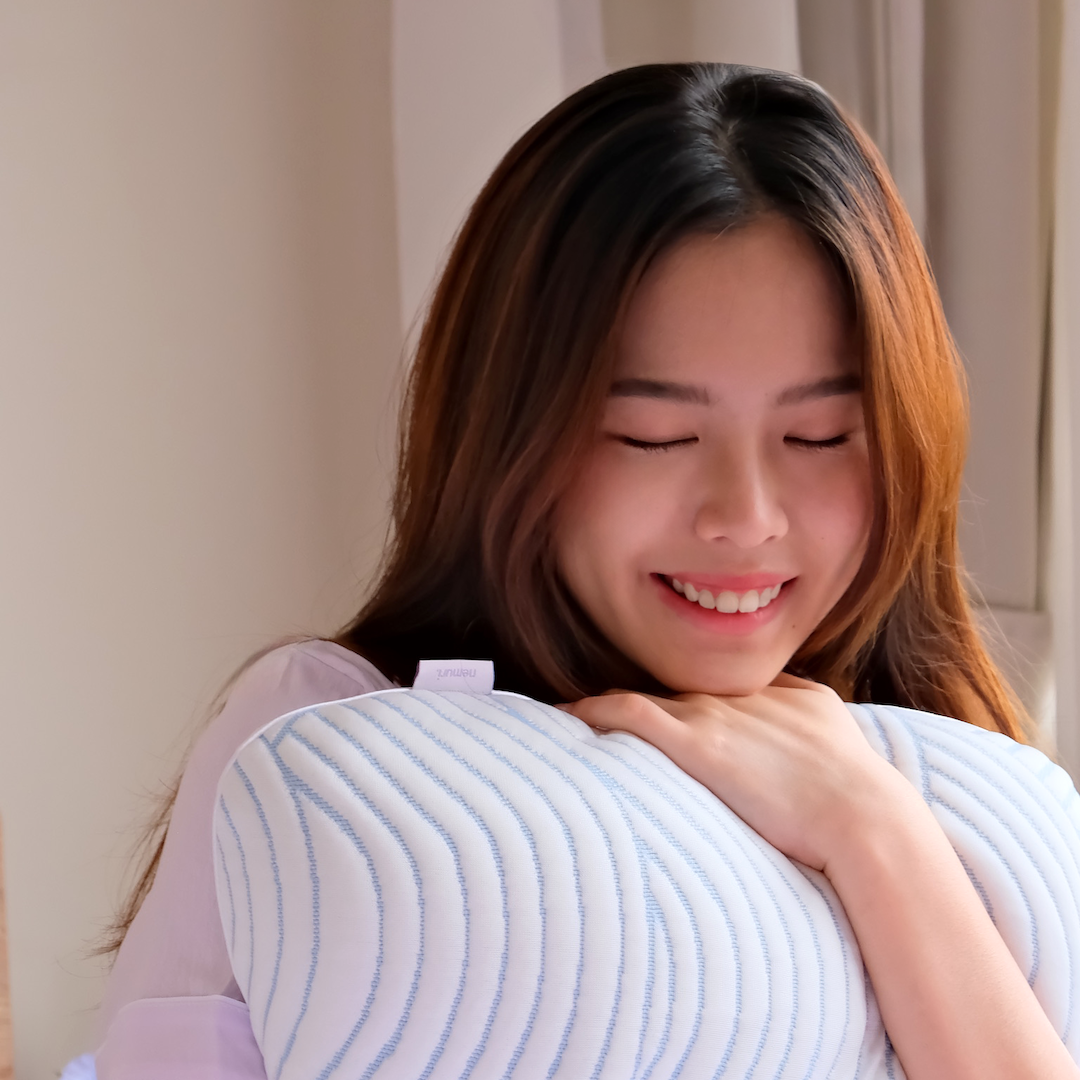 Woman holding a baby wrapped in a light blue nemuri pillow, smiling.