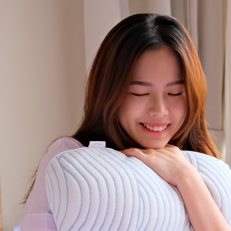 Woman holding a baby wrapped in a light blue nemuri pillow, smiling.