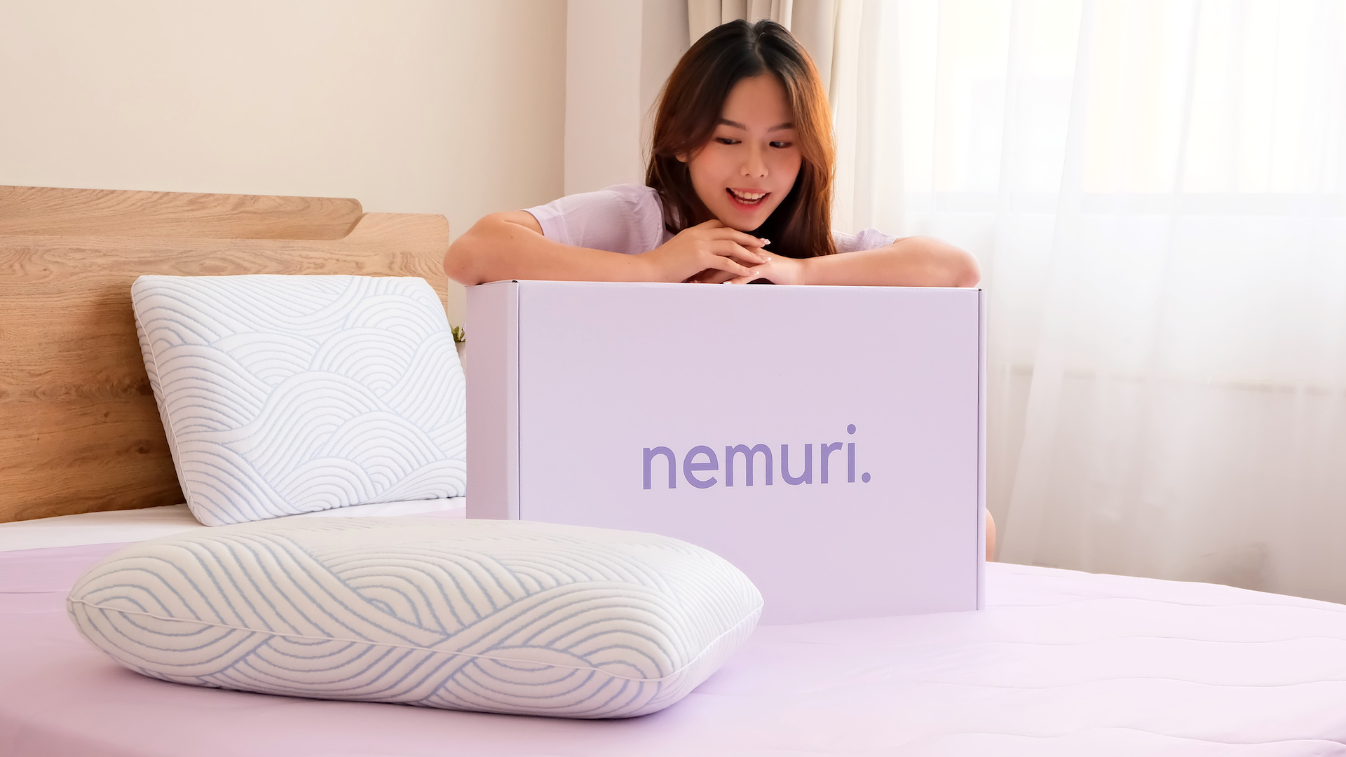 Woman opening a box labeled 'nemuri' on a bed with a pillow in the foreground.
